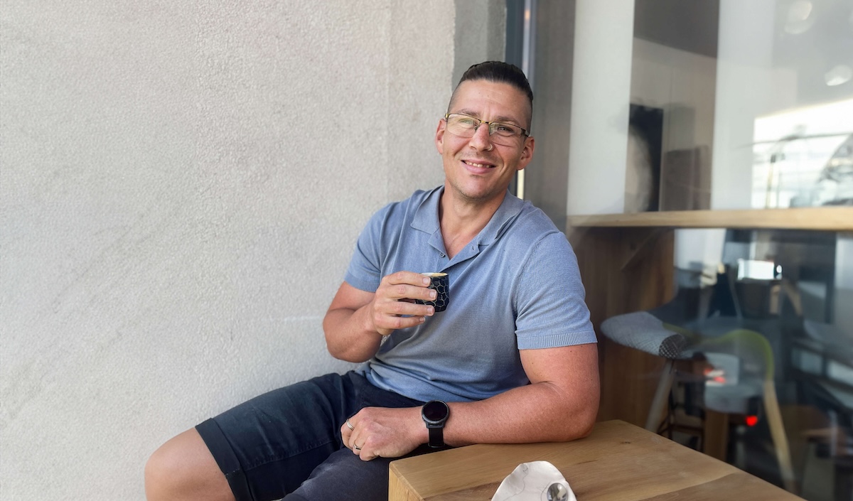 Ricky sitting at cafe smiling with coffee in hand